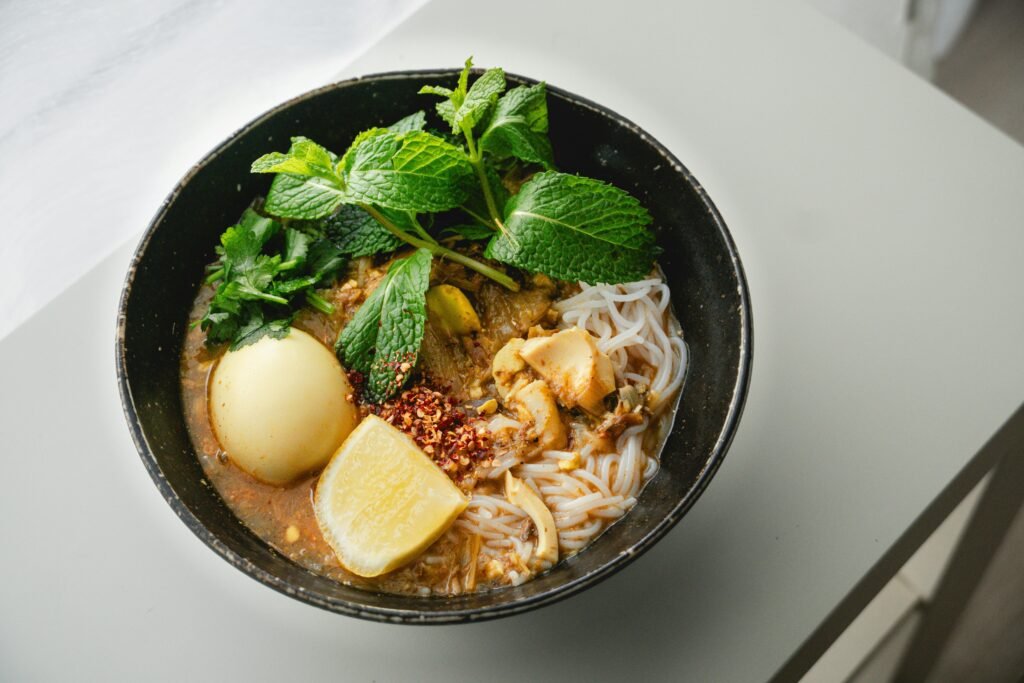Delicious Burmese noodle soup with egg, spices, and fresh mint garnished in a black bowl.