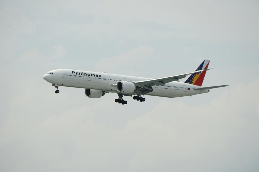 Boeing 777 of Philippine Airlines flying against a cloudy sky.