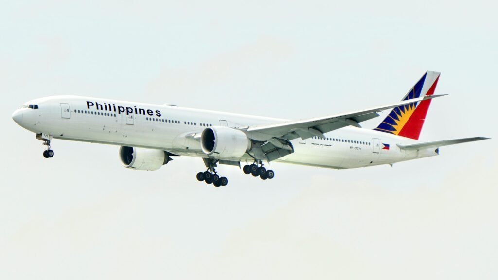A Philippine Airlines Boeing 777 aircraft flying with landing gear lowered against a clear sky.